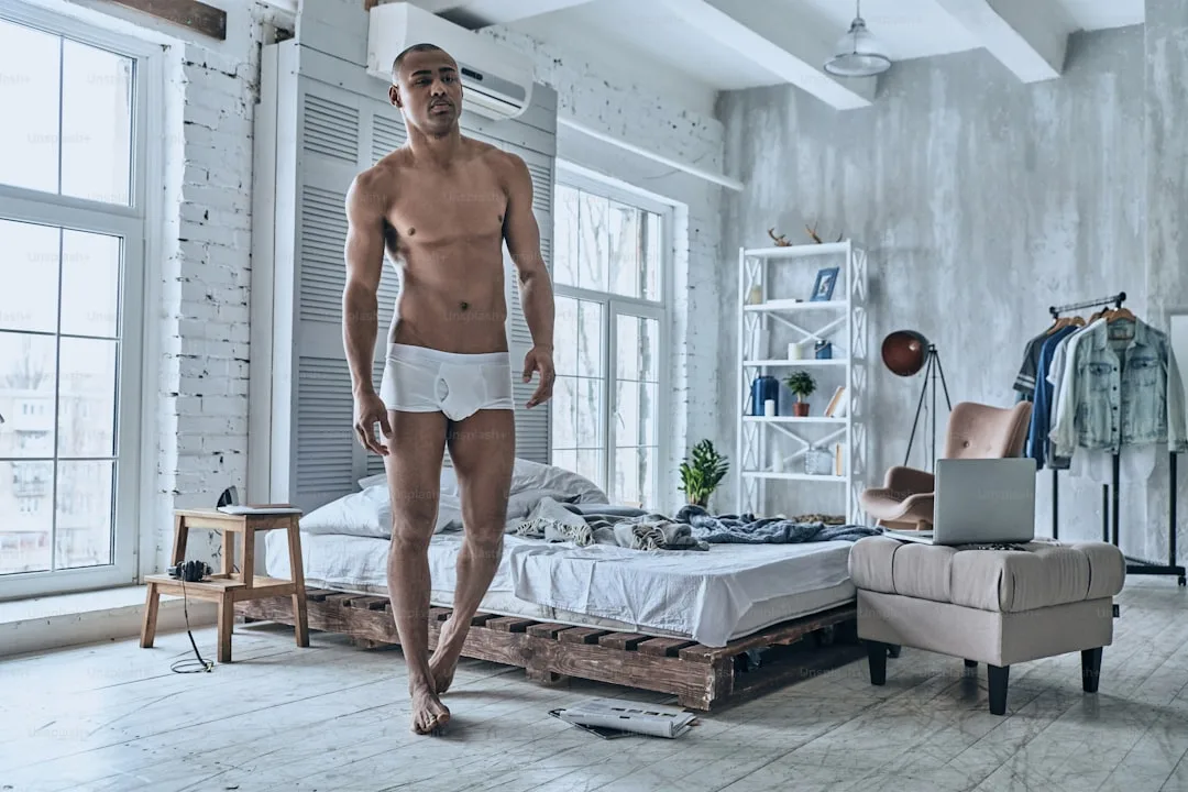 Pleine longueur d’un beau jeune homme africain regardant ailleurs tout en marchant dans la chambre à coucher à la maison